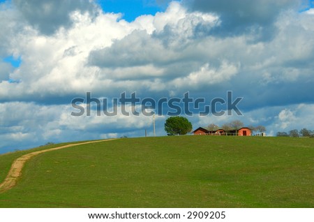 Farmland in California USA, a residential home sits on top of a grassy knoll  against a stunning blue sky with huge puffy white clouds.