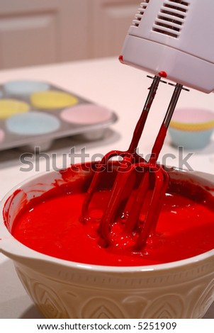 Mixing Cake Batter - A bowl full of red cake batter with an electric mixer.  Cupcake pan in the background.