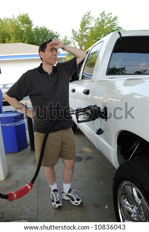 A man pumping gasoline into a pickup truck with a look of surprise at the amount it takes to fill it.