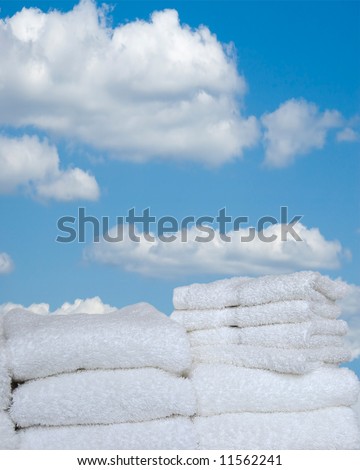 Fresh As Spring - A stack of folded white towels and wash cloths outside against a bright blue sky with white puffy clouds.