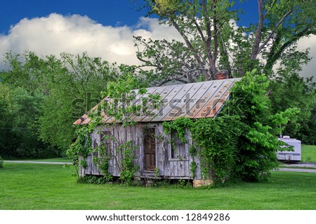 This Old House - A run down house overgrown with vines and weeds with a travel trailer sitting out back.
