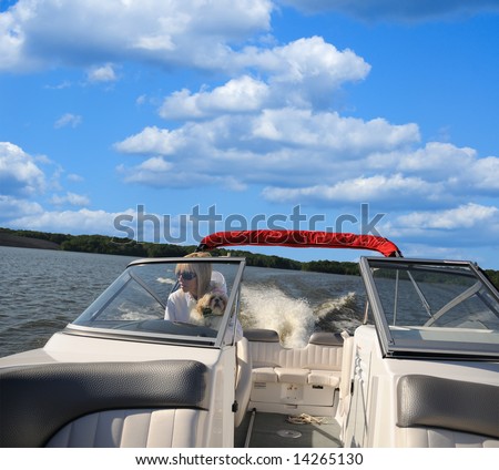 Woman driving a jet boat on a lake in Kentucky, USA while holding her shih tzu puppy.