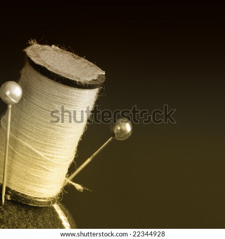 Vintage spool of thread and pins on a pin cushion in sepia, macro shot