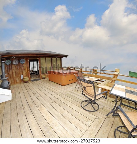 A deck with a hot tub and tables high up with a sky view.  Cabin in the sky, wide angle fisheye view.
