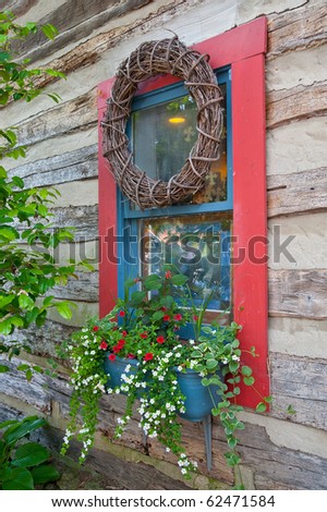 A decorated window on the side of a log home shows dried wreath and flower box decor.