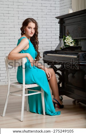 Young elegant woman in dress sitting near piano.