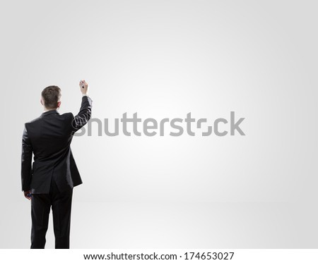 Back view of a businessman about to write something on a white wall.