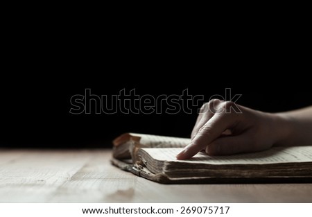 woman finger presses on old bible book in a dark
