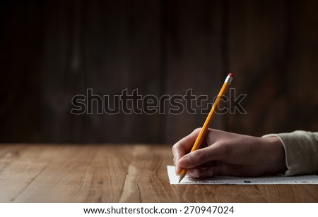 Closeup of woman\'s hand writing on paper over wooden table
