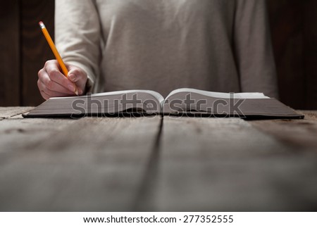 woman hands on bible. she is reading and praying over bible in a dark space over wooden table
