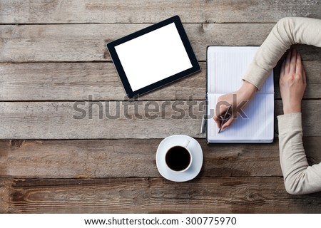 woman writes on a paper with screen of digital tablet next to her. Top angle