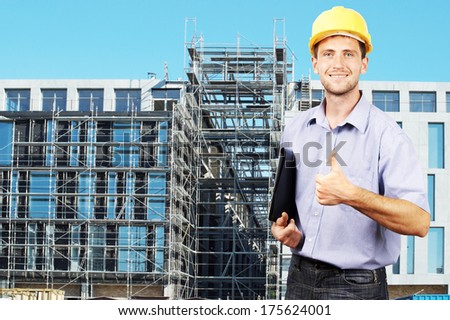 Young smiling businessman in his helmet against the backdrop of the building under construction