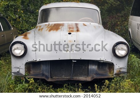 circa 1950 car missing front end parts sitting in weeds
