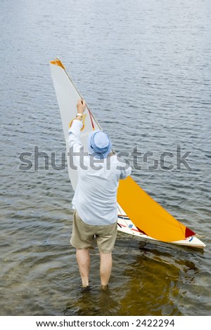 Radio controlled model sailboat on lake being adjusted by senior citizen