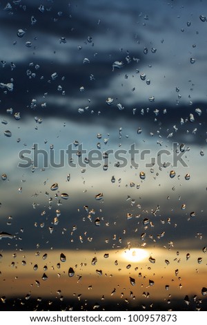 Water drops on a window glass after the rain. The sky with clouds and sun on background. Vertical.