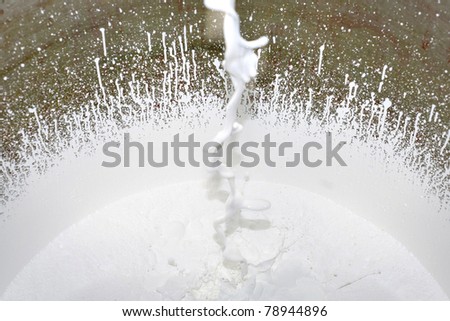 Flow of white paint falls into a bucket