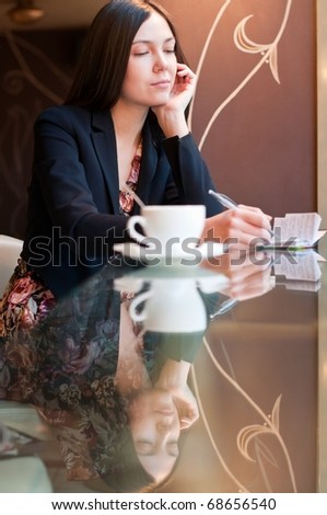 Attractive brunette young woman takes notes sitting in a cafe, shallow DOF, focus on face