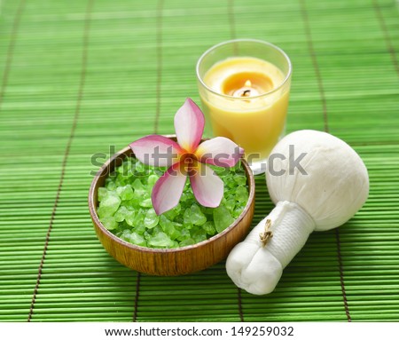 frangipani with salt in bowl with massage ball and candle on green bamboo mat