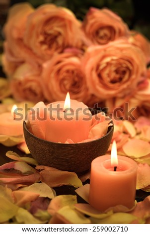 Orange rose petals with candle in bowl and branch rose