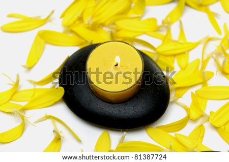 A single burning candle on stone with yellow flower plants