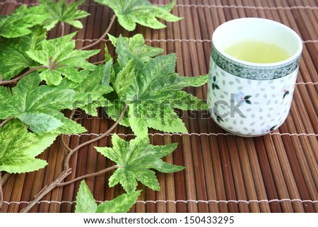 green tea cup on bamboo mat with green maple leaves