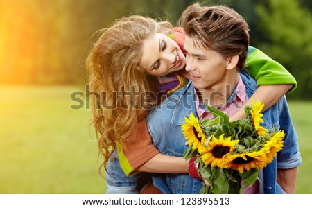 Loving young man hugging his girlfriend with sunflowers in their hands