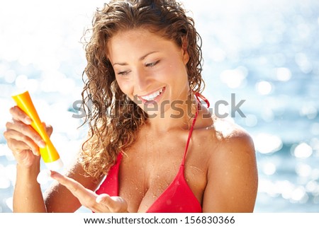 woman applying suntan lotion at the beach smiling