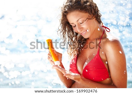 Sunscreen woman. Girl putting sun block on beach holding orange sun tan lotion bottle.