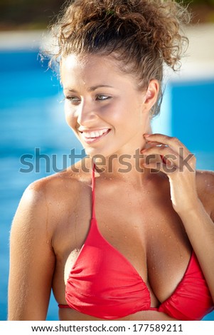 A beautiful sexy young  girl or young woman wearing a bikini and relaxing on the side of a swimming pool.