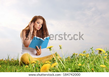 Young beautiful woman on green field and reads book.