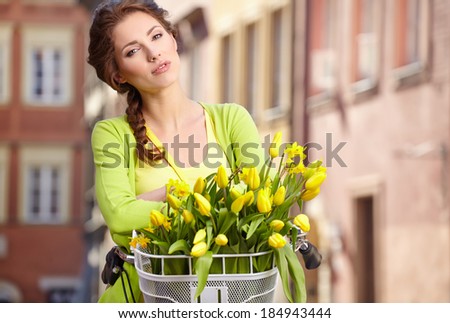 Woman wearing a spring skirt like vintage pin-up holding bicycle with some yellow  flowers in the basket in old town
