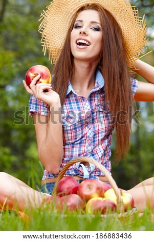 Smiling Young Woman Eating Organic Apple in the Orchard.Basket of Apples.