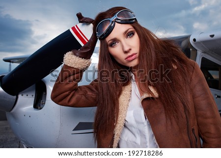 Portrait of young beautiful woman pilot in front of an airplane.