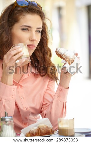 Portrait of beautiful blond woman sitting in outdoors cafe in Italy, drinking coffee and eating croissant.