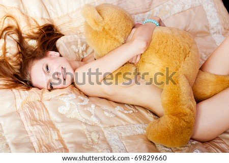 pretty nude woman lies on bed and a teddy bear