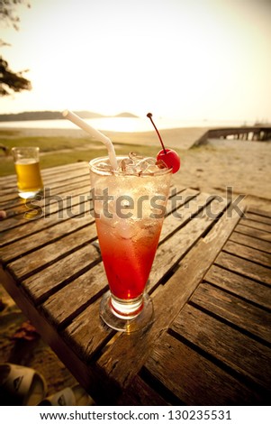 chilling red cocktail on beach, red spirit drink in tall glass decorated cherry by the sea