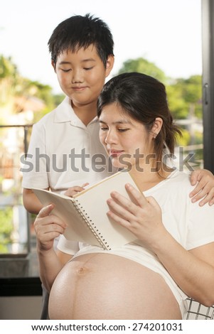 pregnancy care, Young Asian boy sharing times with his mother reading a book