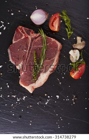 T-bone cut, Red Raw fresh T-bone steak cut put with rosemary herbs seasoning on black background