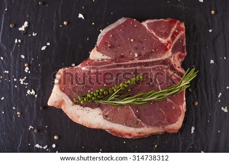 T-bone cut, Red Raw fresh T-bone steak cut put with rosemary herbs seasoning on black background