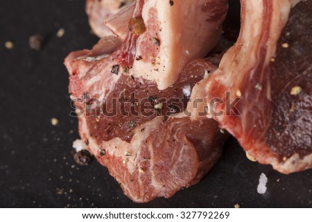 Lamb chop, Raw rack of lamb cut in pieces decorate and seasoning with rosemary tomato herbs and olive oil fork and knife on black stone
