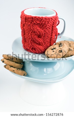 Blue cup with red knitted cover and cookies with chocolate