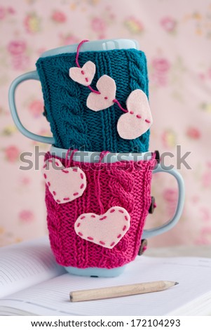 Two blue cups in blue and pink sweater with felt hearts on an notebook