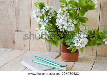 A bouquet of flowering branches of fruit trees and an old notepad with a pencil on a wooden background