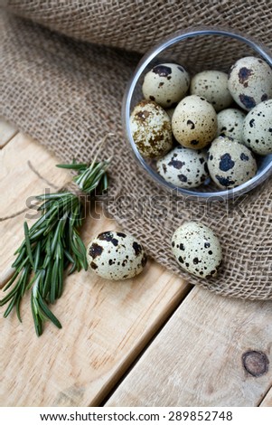 Quail eggs, a bunch of rosemary and burlap are on the unpainted wooden background