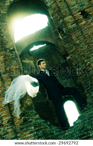 Groom with the bride\'s veil in his hand, in the ruins of a church