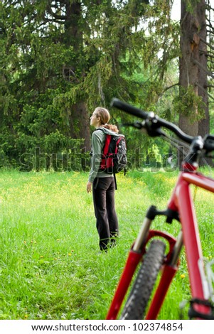 Woman cyclist with bike and backpack among of green nature in spring. Bike are not the focus
