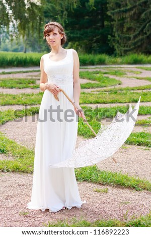 White elegant woman in white dress with decorative umbrella in a vintage style against background green nature