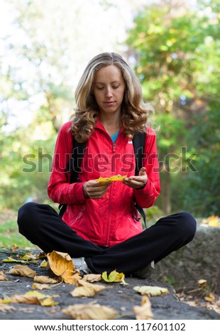 Young woman with backpack in a autumn nature. Enjoying relaxation sitting on the stone