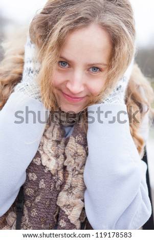 Portrait of a frozen happy young woman in winter clothes heated by wool mittens. Winter outdoor