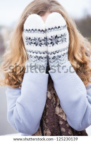 Young girl in winter clothes covered her face with wool mittens. Outdoor